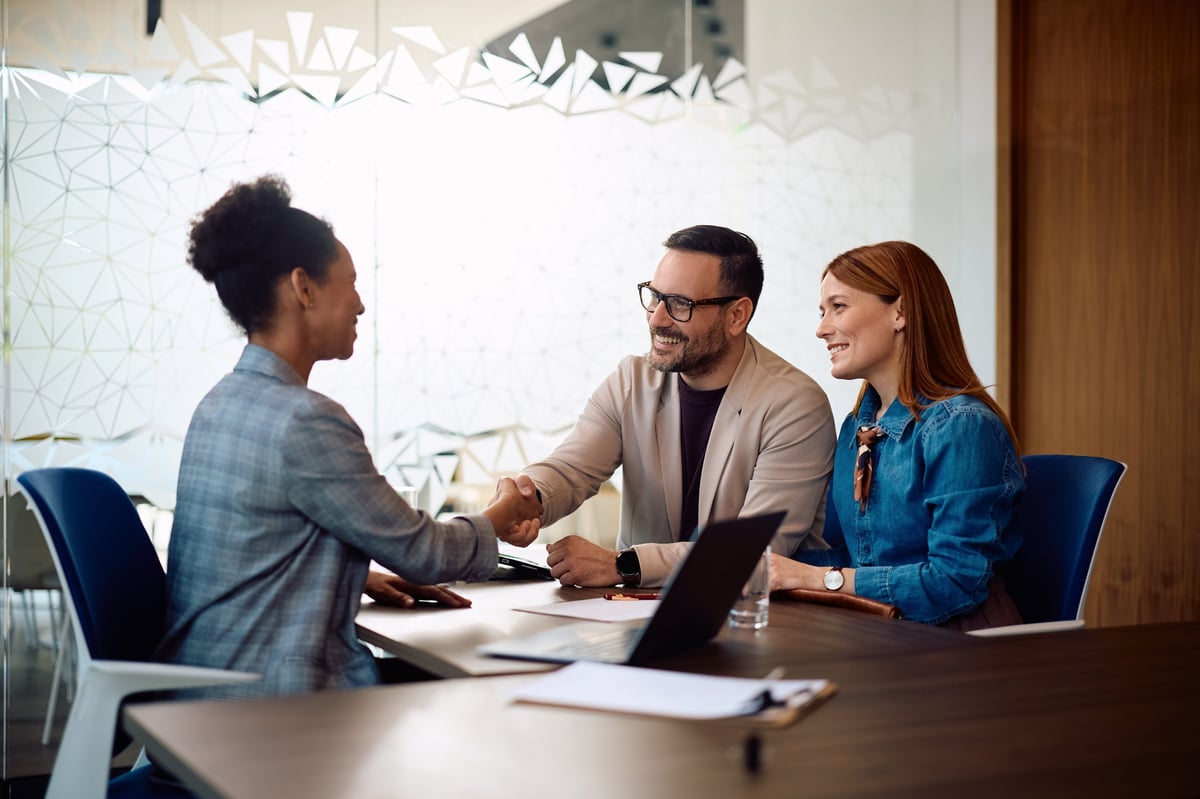 Happy couple shaking hands with their insurance agent in the office. Focus is on man.